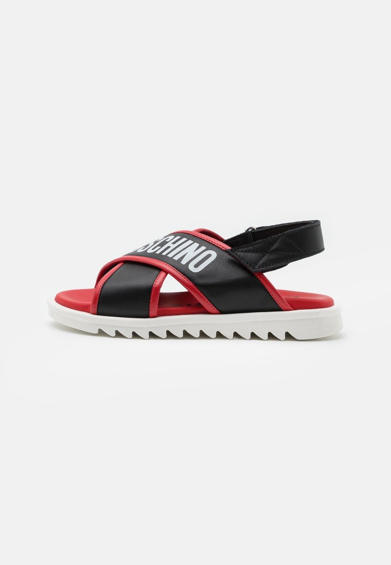 Sandale noire et rouge avec des brides croisées, semelle blanche striée et texte blanc du nom de la marque sur la bride supérieure.