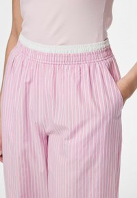 Heledad roosa triibuline püksid valge elastse vöökohtade ja küljetaskutega. Kangas on sile ja kerge ning sellel on vertikaalsed triibud.