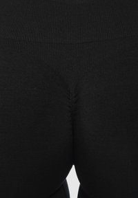 Leggings neri mostrati dalla vita in giù, con un elastico a coste in vita e una texture liscia e elastica in tutto il capo.