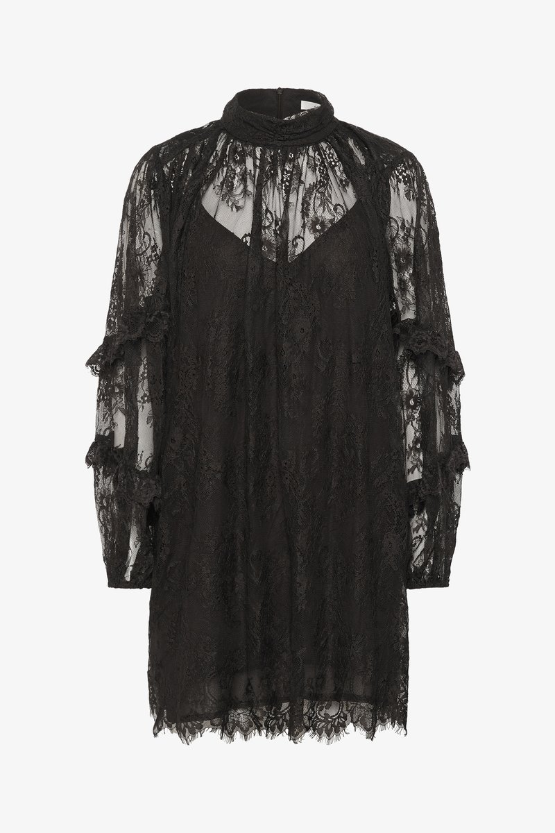 Abito in pizzo nero con maniche lunghe trasparenti, arricciature raccolte sulle spalle, scollatura alta e orlo scallop. Dettagli floreali in pizzo su tutta la superficie.