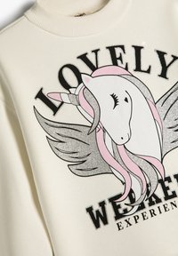 Sudadera color crema con un gráfico de unicornio y detalles en rosa y plata. El texto dice "EXPERIENCIA DE FIN DE SEMANA ENCANTADORA".