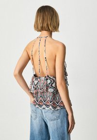 Top halter multicolor con dobladillo con volantes, presenta un diseño sin espalda y tirantes finos. El patrón incluye zigzags en rosa, azul y negro.