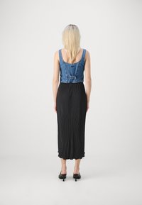 Denim crop topp med tettsittende midje, kombinert med et langt, svart plissert skjørt. Outfit'en har et beltedetalj og en flytende silhuett.
