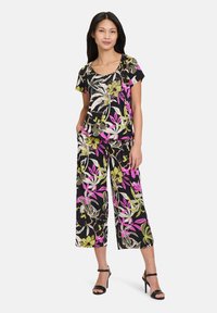 Ensemble floral deux pièces en noir avec des motifs éclatants de rose, jaune et vert. Comprend un haut à encolure dégagée et un pantalon large. Fini en tissu lisse.