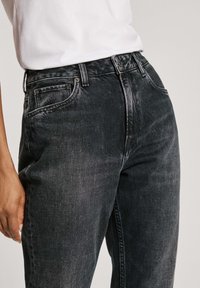 Högmidjade svarta jeans med en blekt tvätt, klassisk fem-ficksdesign och en robust knapp- och dragkedjestängning fram. Slät textur.