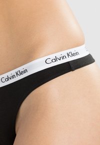 String noir en coton avec une ceinture élastique blanche arborant le logo "Calvin Klein" en noir. Texture lisse, design minimaliste.