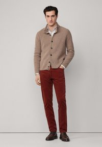 Hnedý textúrovaný cardigan s golierom, predným zapínaním na gombíky, so strihom na mieru, skombinovaný s hrdzavými zamatovými nohavicami a tmavo hnedými topánkami.