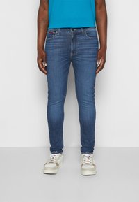 Jeans ajustados de mezclilla azul oscuro con una textura suave, que cuentan con un diseño clásico de cinco bolsillos y detalles sutiles de costura. Combinados con zapatillas blancas.