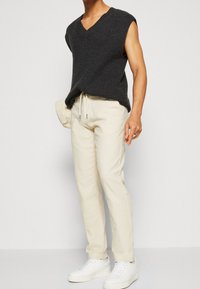 Top senza maniche grigio scuro a maglia con scollatura a V, abbinato a pantaloni leggeri beige e sneaker bianche, dotati di vita con coulisse.