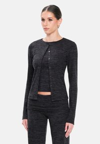 Cardigan nero a maglia con scollatura rotonda, chiusura frontale con bottoni e maniche lunghe, abbinato a una maglietta aderente e pantaloni coordinati.