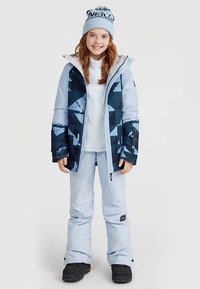 Slēpošanas tērps ietver zilu jaku ar ģeometriskiem rakstiem, gaiši zilas bikses un gaiši zilu cepuri ar melnu logotipu.