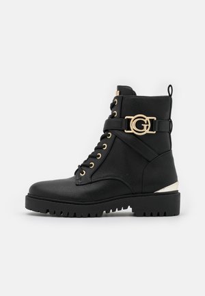 Bottines en cuir noir avec quincaillerie dorée, dotées de lacets épais, d'une sangle latérale décorative et d'une surface texturée. Semelle épaisse avec crampons.