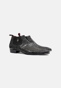 Botas de tobillo de cuero negro con diseño en relieve de flores, puntera afilada, paneles laterales elásticos y un tacón bajo apilado. Presenta herrajes decorativos.
