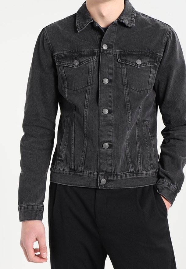 Homme portant une veste en denim noire ajustée avec des fermetures à boutons, des poches poitrine à rabat et des poches latérales, assortie à un pantalon noir.