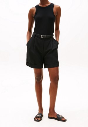 Top de tirantes negro con textura acanalada combinado con pantalones cortos negros de cintura alta con bolsillos laterales y cinturón. Sandalias negras tipo slide completan el conjunto.