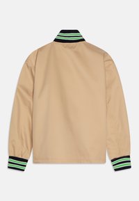 Giacca beige con un colletto e polsini a strisce nere e verdi. Presenta una texture liscia e un design semplice e minimalista.