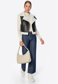 Chaleco negro de cuero sintético con forro de pelaje blanco, combinado con un suéter de cuello alto crema, jeans azul de cintura alta, bolso beige y zapatillas blancas.