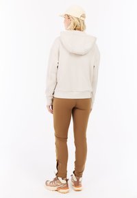 Lichtbeige hoodie met een ontspannen pasvorm, gecombineerd met strakke bruine broek en bruine wandelschoenen met witte accenten.