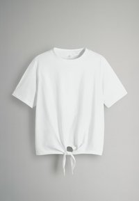 Hvid bomulds t-shirt med korte ærmer, der har en knyttet sløjfe ved fronten af kanten. Stoffet ser glat og letvægtigt ud.