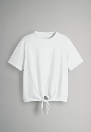 Biela bavlnená tričko s krátkymi rukávmi, s uzlom na prednom leme. Tkanina vyzerá hladko a ľahko.