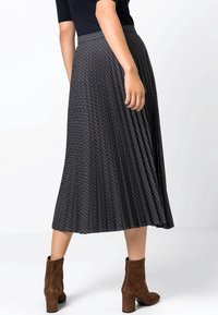 Jupe midi plissée en tissu sombre avec un motif géométrique de carrés bleus et orange. Associée à des bottes chelsea en suède marron.