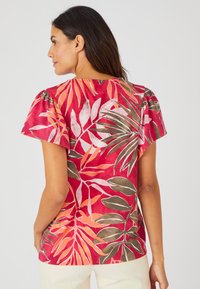 Top de manga corta rojo con estampado floral que presenta un patrón de hojas tropicales en rosa, naranja y verde. Tejido suave con un corte relajado y cuello redondo.