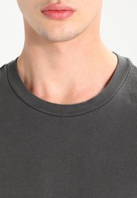 Šedé bavlněné triko s krátkým rukávem a hladkým povrchem. Výstřih je zdobený žebrovaným lemem a látka se dobře přizpůsobuje postavě, bez vzorů.