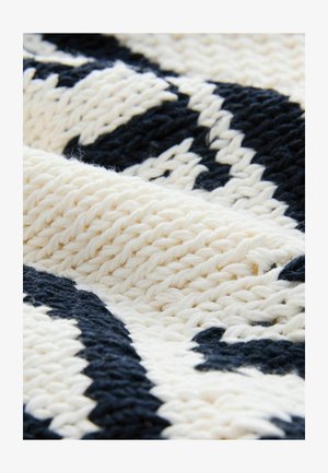 Geweven textiel met een crèmekleurig en marineblauw patroon, dat een textuur oplevert met verweven draden en contrasterende kleuren.