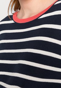 Granatowy sweter w białe poziome paski. Posiada koralowy, prążkowany dekolt. Materiał wydaje się być dziany o miękkiej teksturze.