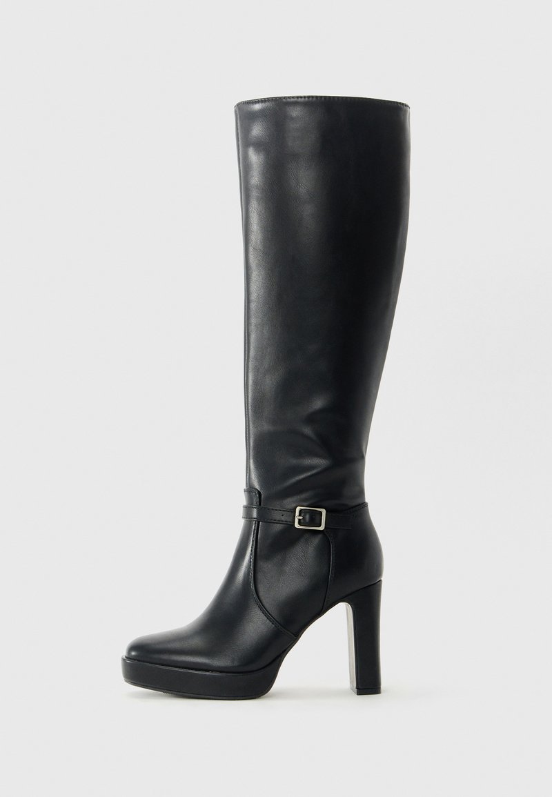Bota alta de cuero negro con tacón bloque, suela de plataforma y correa de hebilla lateral, fotografiada contra un fondo claro y liso.