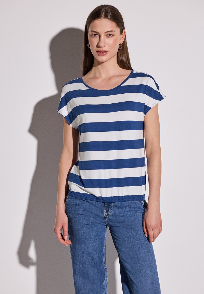 Top de manga corta a rayas azul y blanca en tejido suave, con un escote redondo y un corte relajado. Combinado con unos vaqueros azul.
