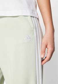 adidas Sportswear ESSENTIALS 3-STRIPES LOOSE-FIT - Tepláky - linen green