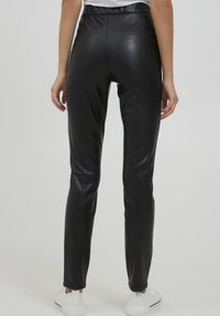 Zwarte neplederen leggings met een aansluitend ontwerp, een gladde textuur, hoge tailleband en rechte pijpen. Geen zichtbare hardware of patronen.