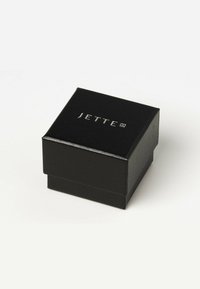 Sort tekstureret smykkeboks med firkantet form og blank finish, der har det indgraverede mærkenavn "JETTE" i sølv på toppen.