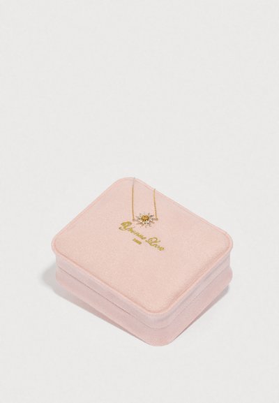 Růžová sametová šperkovnice se zlatým nápisem, obsahující zlatý náhrdelník s motivem hvězdného výbuchu s drahokamy.