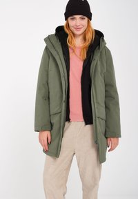 Veste extérieure verte avec une capuche et fermeture à boutons, superposée à une veste intérieure noire et un haut rose clair. Comprend deux poches avant.