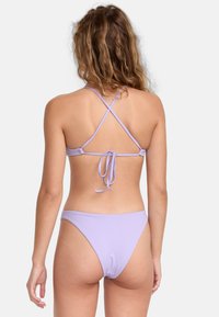 Sada lilac bikiny s křížovým designem, tenkými nastavitelnými ramínky a detaily na zavazování na zádech. Látka má hladkou strukturu.