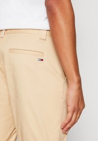 Beiga bomullsbyxor med tight passform. Har en bakficka och en liten tri-färgad logotypapplikation. Slät textur med sydda sömmar.