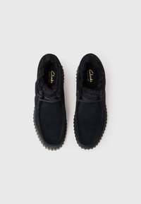 Crni nubučasti Clarks Signature penny loaferi s krznom unutra i gumenim potplatima s čepovima, prikazani odozgo na bijeloj pozadini.