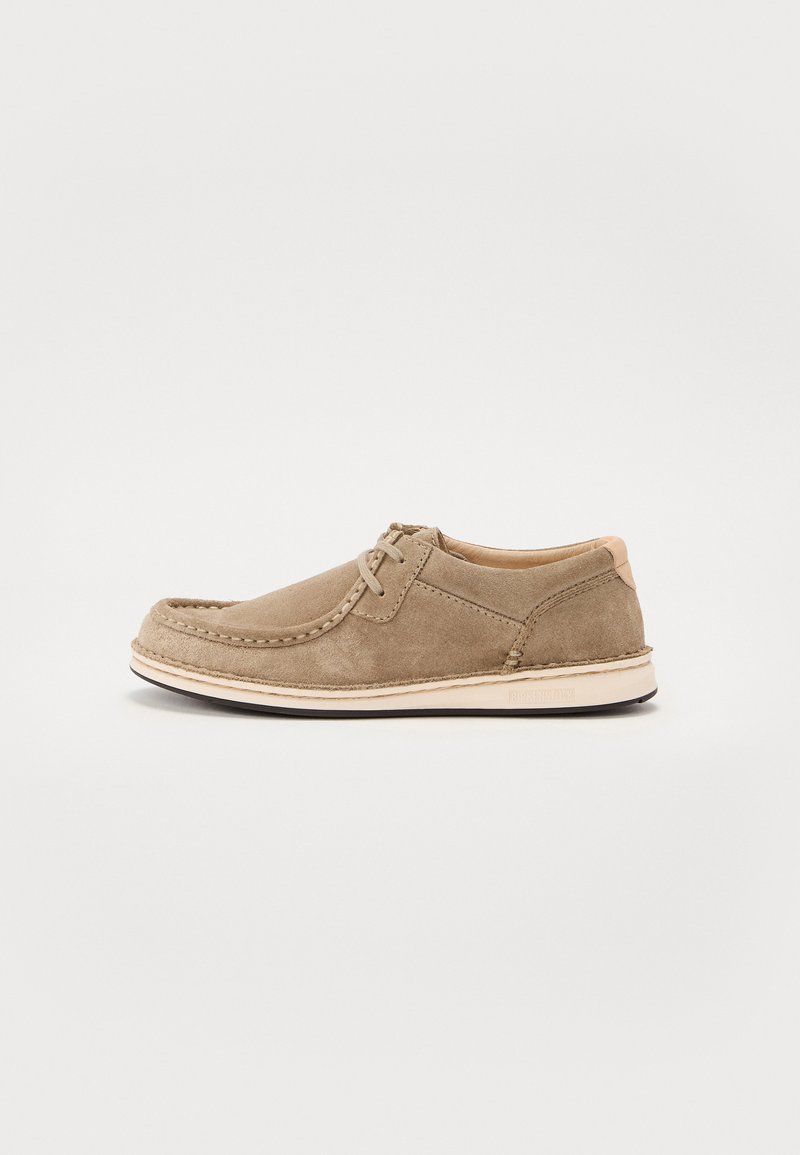 Scarpa da uomo in suede marrone con punta rotonda, cuciture decorative, design con lacci e suola in gomma bianca. Texture liscia con accenti minimi.