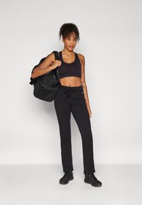 Black athletic bra and sweatpants with drawstring; textured black backpack slung over shoulder; black sneakers; minimalistic design.