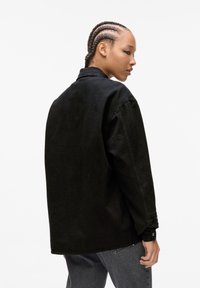 Black denim jacket with a loose fit, single button cuffs, and a classic collar. Textured fabric with a clean, casual design.
