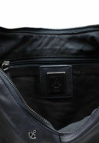 Interno della borsa in pelle blu navy con chiusura a zip, rivestimento in tessuto morbido, un piccolo logo dell'ancora e un'etichetta in pelle con marchio.