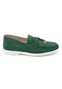 Green suede loafers with a flat white sole, featuring a decorative bow and silver accent on the front. Smooth texture and streamlined shape.