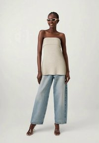 Beige ribbed strapless top paired with light blue wide-leg jeans. Model wearing clear framed sunglasses and open-toed sandals.