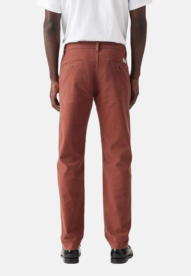 Røde bomuldsbukser med lige pasform, der har to baglommer og en syet labeldetalje, båret med en ensfarvet hvid t-shirt.