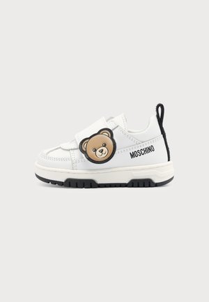 Basket blanche pour enfants avec semelle noire, décoration ours en peluche sur la bride et logo "Moschino" sur le côté.