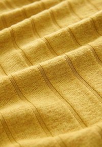 Hořčičně žlutá látka s texturovaným žebrovým vzorem. Obsahuje horizontální pruhy a hladký povrch, ukazující pletený materiál a viditelné švy.