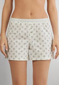 Lichtjes gehalte katoenen shorts met een bloemmotief in zachte crèmekleuren. Heeft een elastische tailleband en drie knopen aan de voorkant.