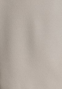 Beiger Stoff mit einer weichen, strukturierten Oberfläche, die ein dezentes, gleichmäßiges Muster aufweist. Das Material wirkt glatt und leicht.